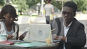African man and female colleague working together, using gadgets during meeting at a cafe