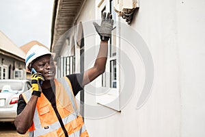 an african man holding a cell phone to his ear while wearing safety clothing and working