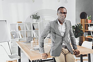 african man leaning on table and looking at camera at office