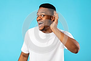 African Man Listening Holding Hand Near Ear On Blue Background