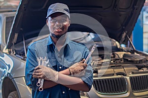 African man mechanic in uniform with crossed arms and wrenches standing at the car repair station