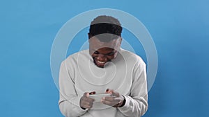 an African man with passion plays on a mobile phone standing on a blue background
