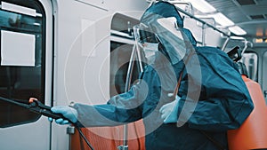 African man with protective suit , face shield, mask and gloves disinfecting interior of the train. Prevention of the