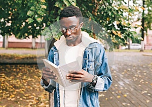 african man reading book in autumn city park