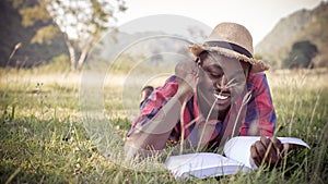 African man reading a book on the grass happily on vacation