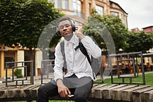 African man resting on bench and listening music in headphones.