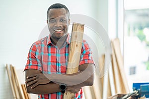 A african man Satisfied cheerful smiling with apron woodmaster is standing near desktop with crossed arms in his workshop,