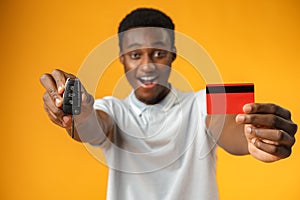 African man showing car key and credit card over yellow background