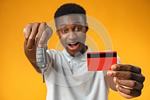 African man showing car key and credit card over yellow background