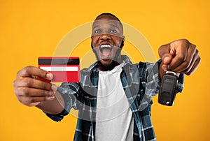 African Man Showing Car Key And Credit Card, Yellow Background