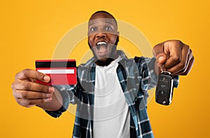 African Man Showing Car Key And Credit Card, Yellow Background
