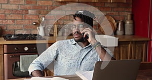 African man sit at table with laptop talking on phone