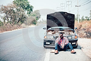 African man sits with his hand over his head as his car breaks down on the road