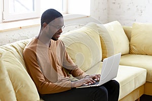 African man sitting on couch typing business letter on laptop