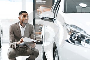 African Man Sitting Near New Vehicle Checking Auto In Store