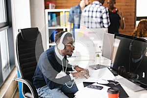 African man is sitting at the table and staring at the screen of the computer