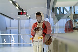 African man with smartphone in airport terminal, young black guy traveler waiting for plane boarding