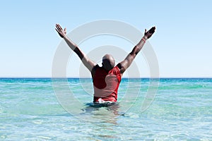 African man standing in sea with his hands raised