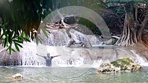 African man standing under the mountain river waterfall, rose arms up and enjoying the splashing Nature power. Concept of