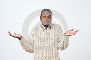 african man in sweater shrugs shoulders with confusion