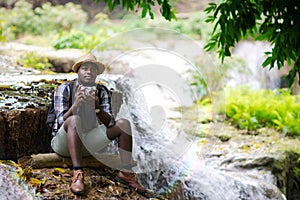 African Man Traveller holding a film camera with backpack sitting and relaxing freedom at the waterfall