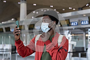 African man using face id feature on smartphone in medical mask in airport at covid-19 quarantine