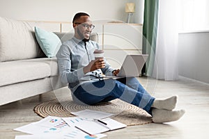 African Man Using Laptop Sitting On Floor Working At Home