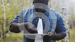 An african man using the tablet in the forest. wireless or future technology concept.