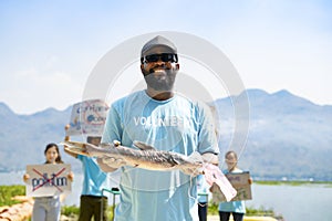 african man volunteer wear sunglasses and hat holding a fish died from eat a garbage plastic bag