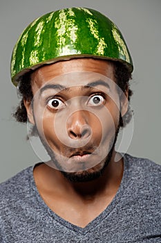 African man with watermelon on head fooling over grey background.