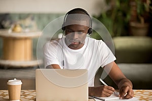 African man wearing headphones watching webinar making notes study online