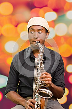 African man wearing sixpence hat and dark shirt playing saxophone, facing camera
