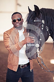 African Man wearing sunglasses near black horse in hangar