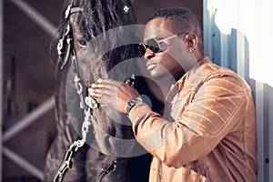 African Man wearing sunglasses near black horse in hangar