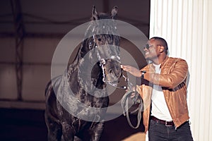 African Man wearing sunglasses near black horse in hangar