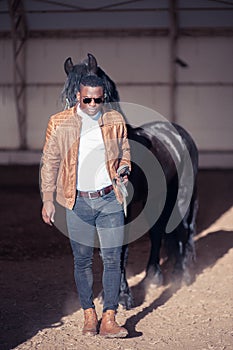 African Man wearing sunglasses near black horse in hangar