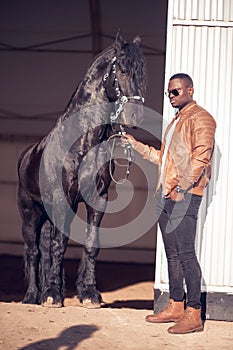 African Man wearing sunglasses near black horse in hangar