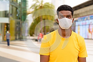 African man wearing yellow t-shirt and face mask to protect from Covid-19 coronavirus outdoors in city