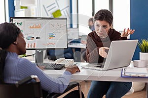 African manager with mask working checking graphs, coworker holding laptop