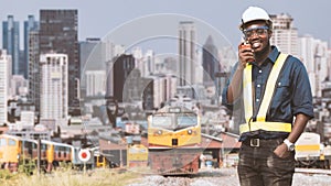 African mechanical engineer talking with radio communication or walkie talkie to maintain train in city center with tall buildings