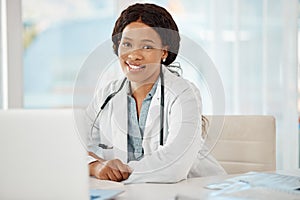 African medical doctor working at a hospital, planning on a laptop and sitting at a desk in an office. Portrait of a