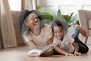 African mom reading book laughing with child son at home