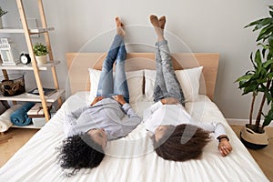 African mom and teen daughter lying on bed legs up