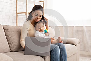 African Mom Working On Laptop Holding Baby Sitting At Home