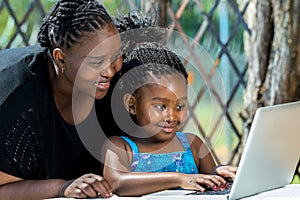 African mother and child looking at laptop outdoors.