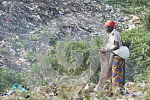 African mother collecting recyclables in trash. Mother with baby in sling collects recyclables from garbage