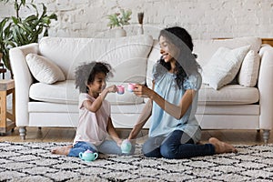 African mother and daughter holds toy tea cups playing indoor