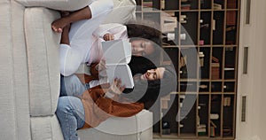 African mother and daughter sitting on couch reading a book