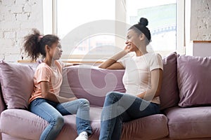 African mother and daughter talking sitting on couch at home