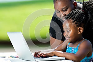 African mother helping kid on laptop.